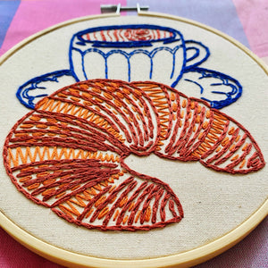 Embroidery hoop with a croissant and coffee cup design on a checkered fabric background