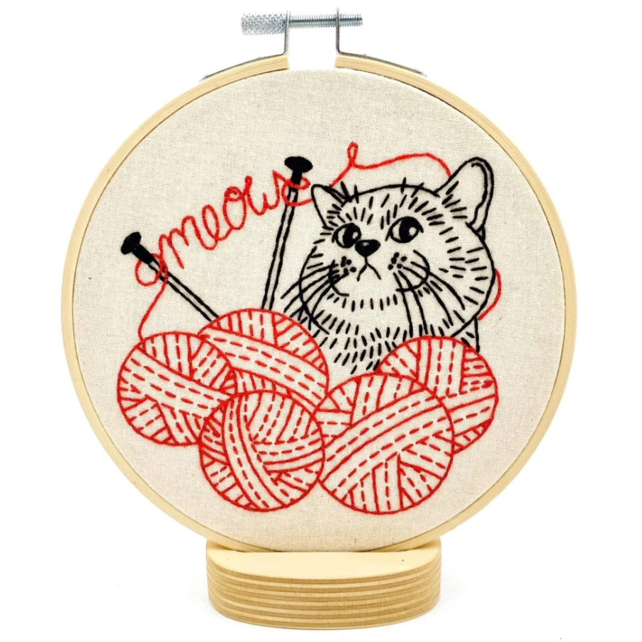 Finished embroidery hoop featuring a black and red stitched design of a cat with five balls of yarn, knitting needles, and script that says "meow"