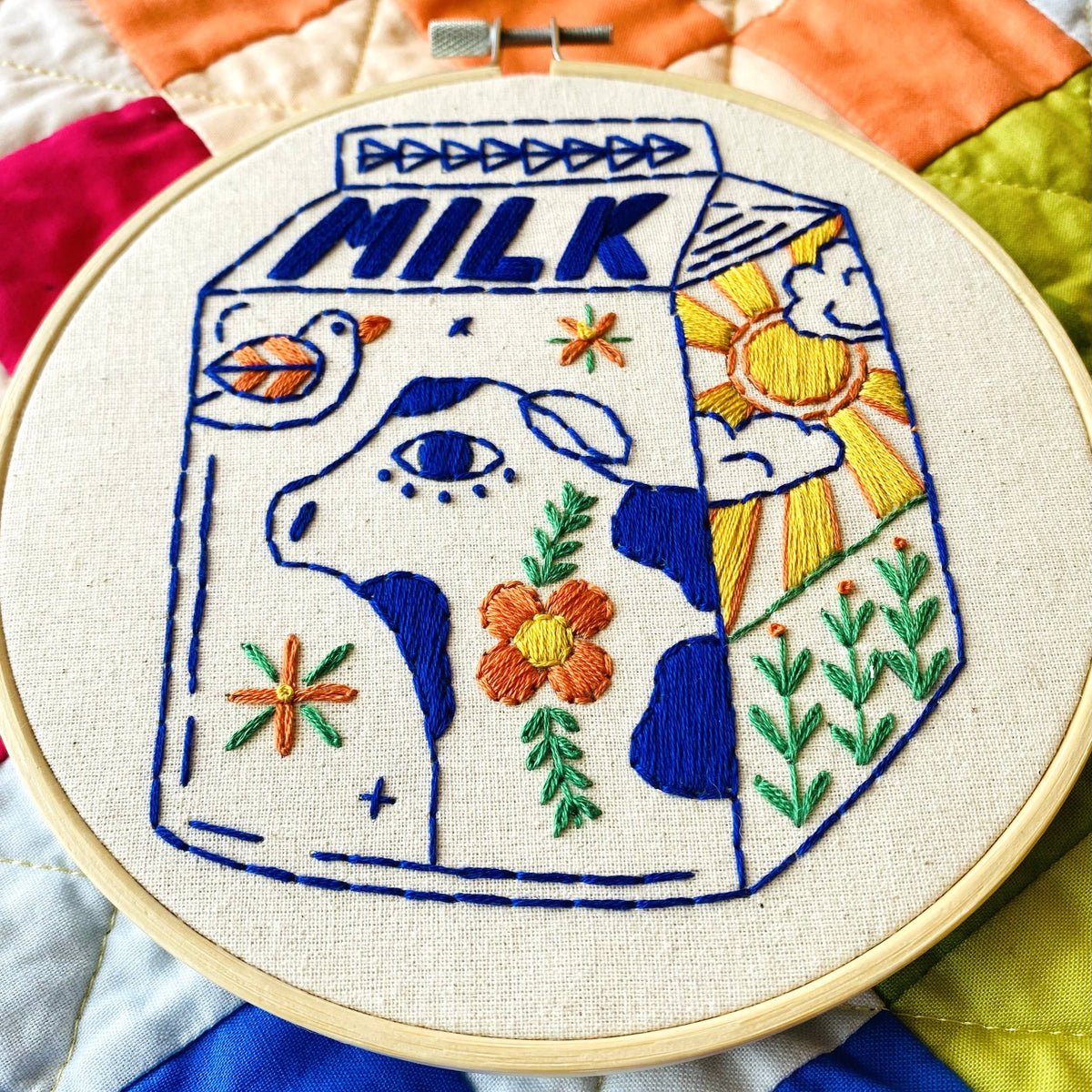 Embroidery hoop with a colorful milk carton design on a multicolored quilted background