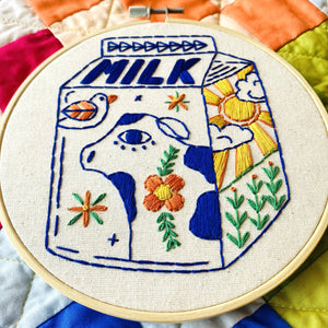 Embroidery hoop with a colorful milk carton design on a multicolored quilted background