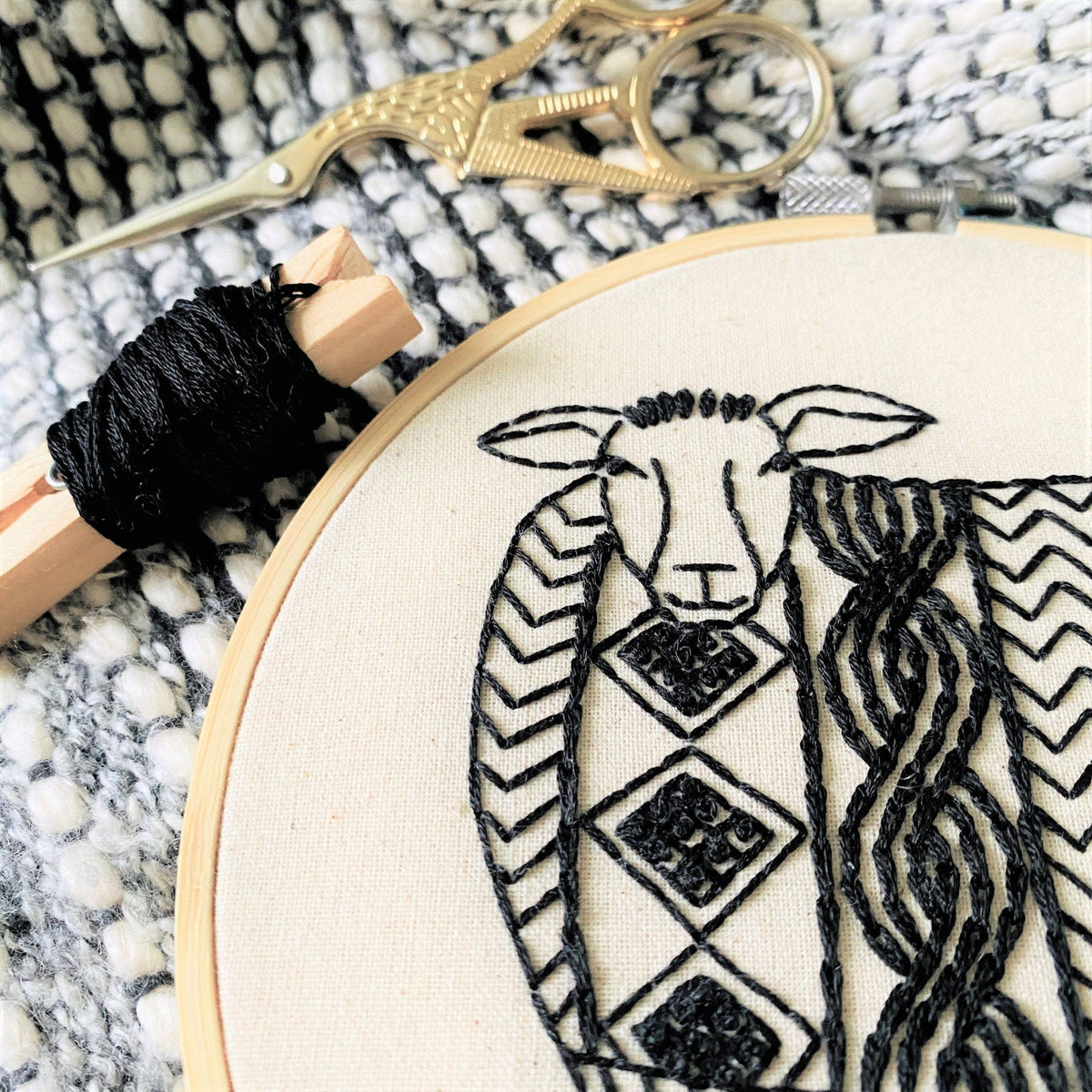Embroidery hoop with black thread and scissors on a marble surface