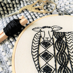 Embroidery hoop with black thread and scissors on a marble surface