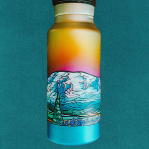 A rainbow water bottle with the Mt. Rainier infinity sticker on it against a blue background