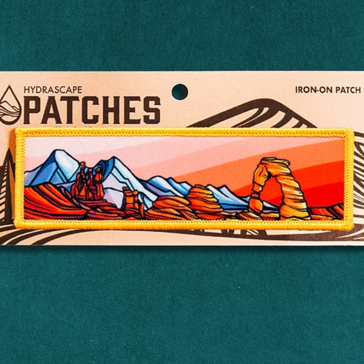 Packaging of a mountain-themed iron-on patch by Hydrascape Patches on a teal background.