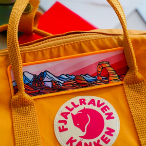 Yellow bag with a colorful design and Fjällraven Kånken logo featuring the Hydrascape Arches patch