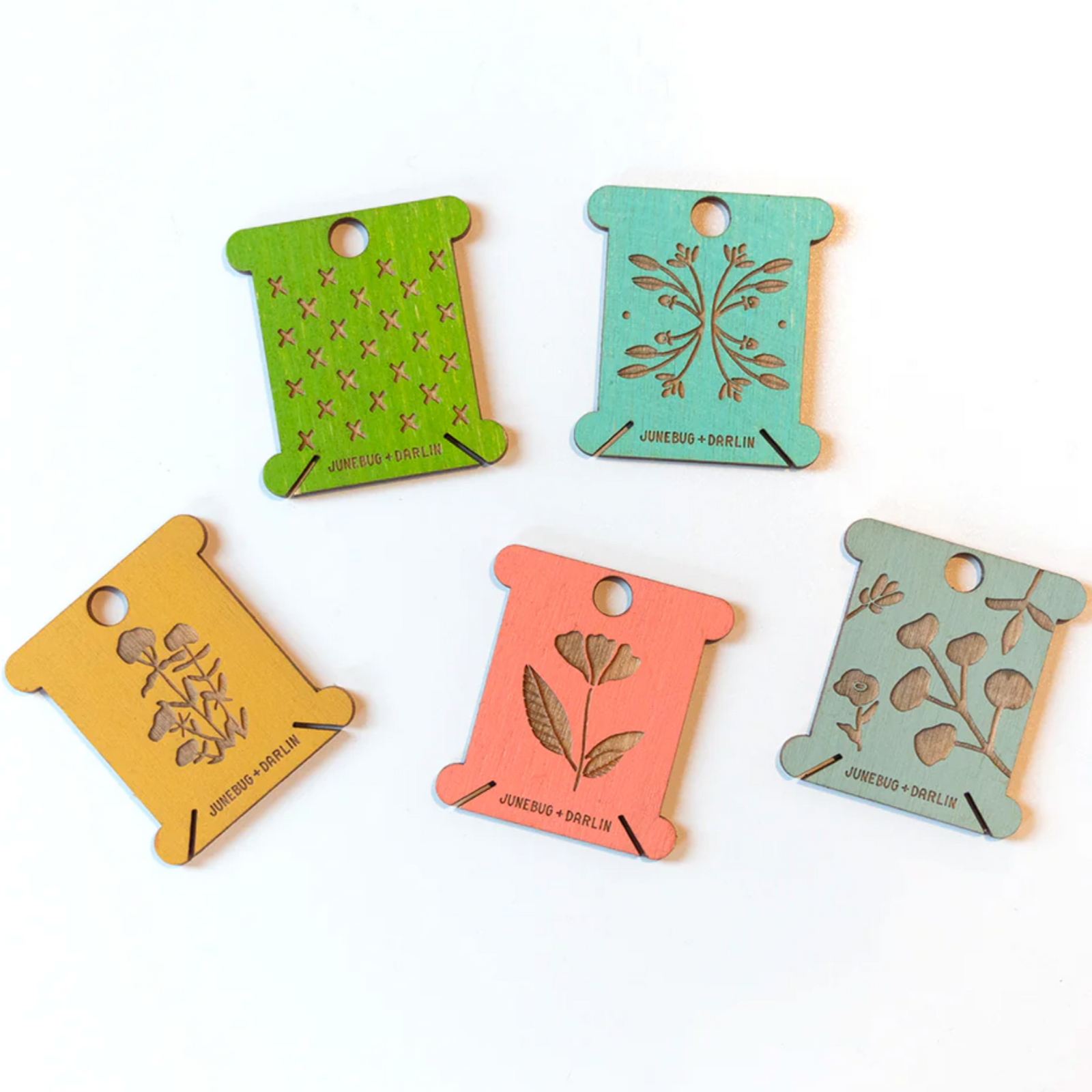 Examples of the floss bobbins you might receive in your random pack of five floss holders from Junebug and Darlin. This batch is spring green, teal, mustard yello, coral and sage green. Most of these have floral designs engraved in them. 