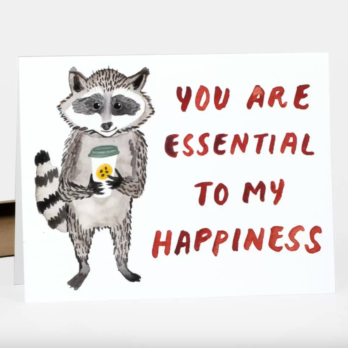 Card with a raccoon holding a coffee cup, text 'You are essential to my happiness' on a white background.