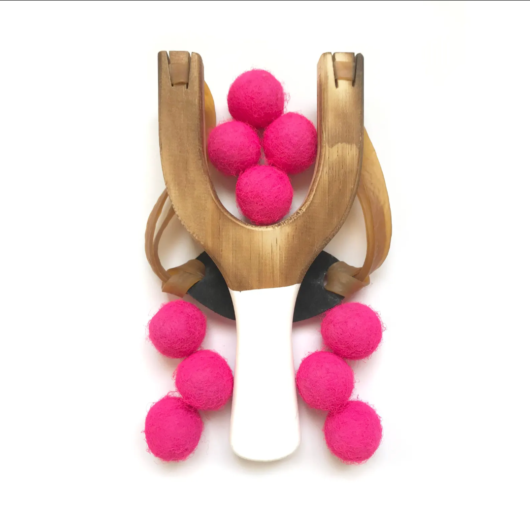 Wooden slingshot with neon pink balls on a white background