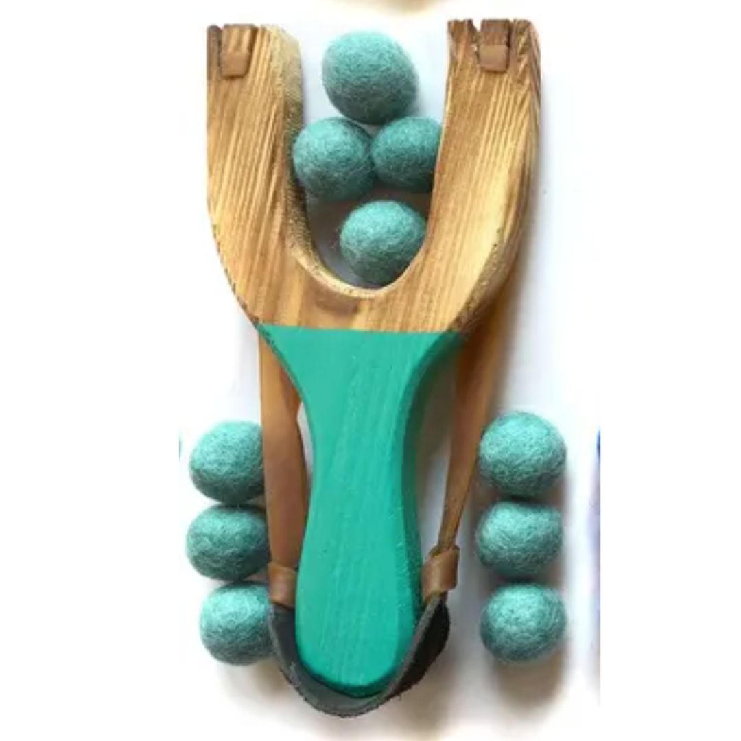 Wooden slingshot with teal felt balls on a white background