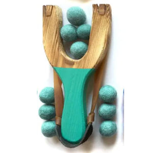 Wooden slingshot with teal felt balls on a white background