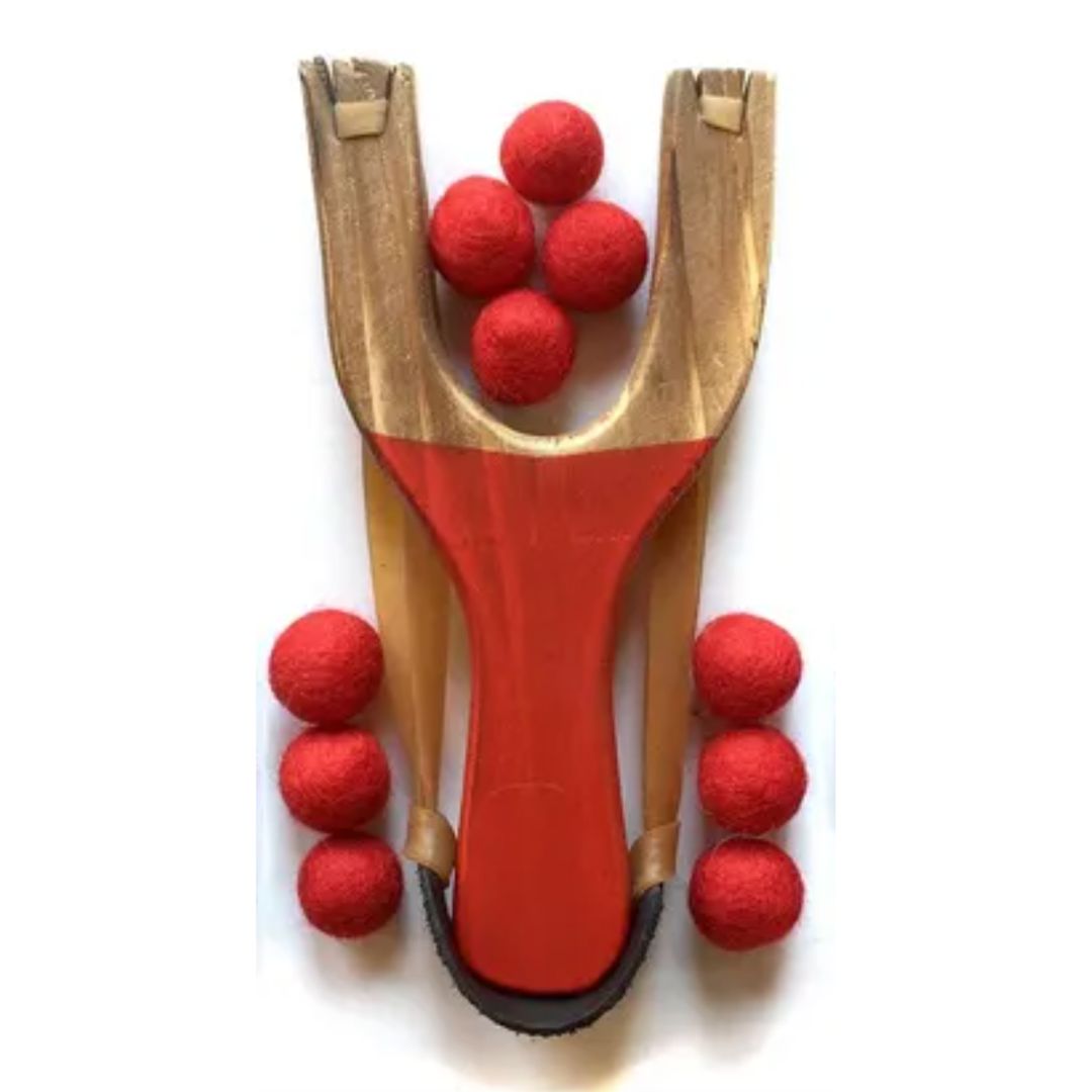 Wooden slingshot with red felt balls on a white background