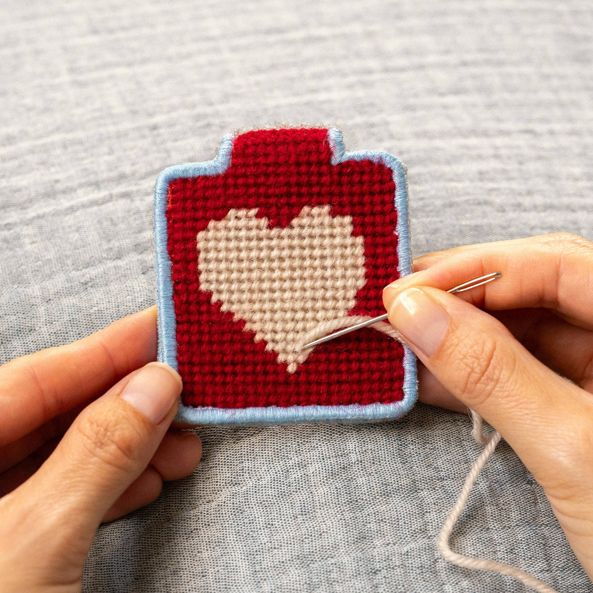 Hand stitching a needlepoint keychain with a heart design. 
