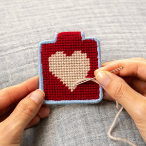 Hand stitching a needlepoint keychain with a heart design. 