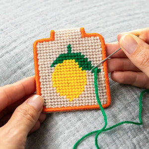 Hand stitching into a needlepoint keychain with a lemon design.
