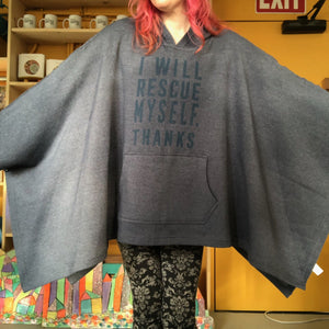 Person wearing a blue poncho with text that says "I will rescue myself, thanks", standing in a room with shelves and an exit sign.