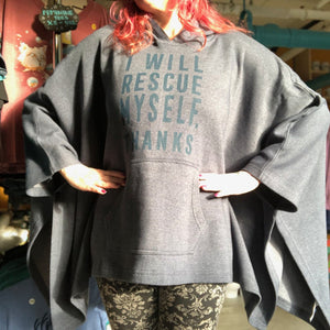 Person wearing a blue hooded poncho with text that says, "I will rescue myself, thanks" in a store setting. 