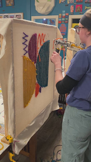 Person using a tufting gun to create an art piece. 