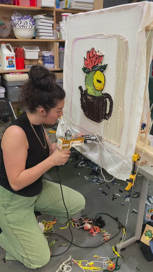 A person is using a tufting gun to create a wall hanging. 