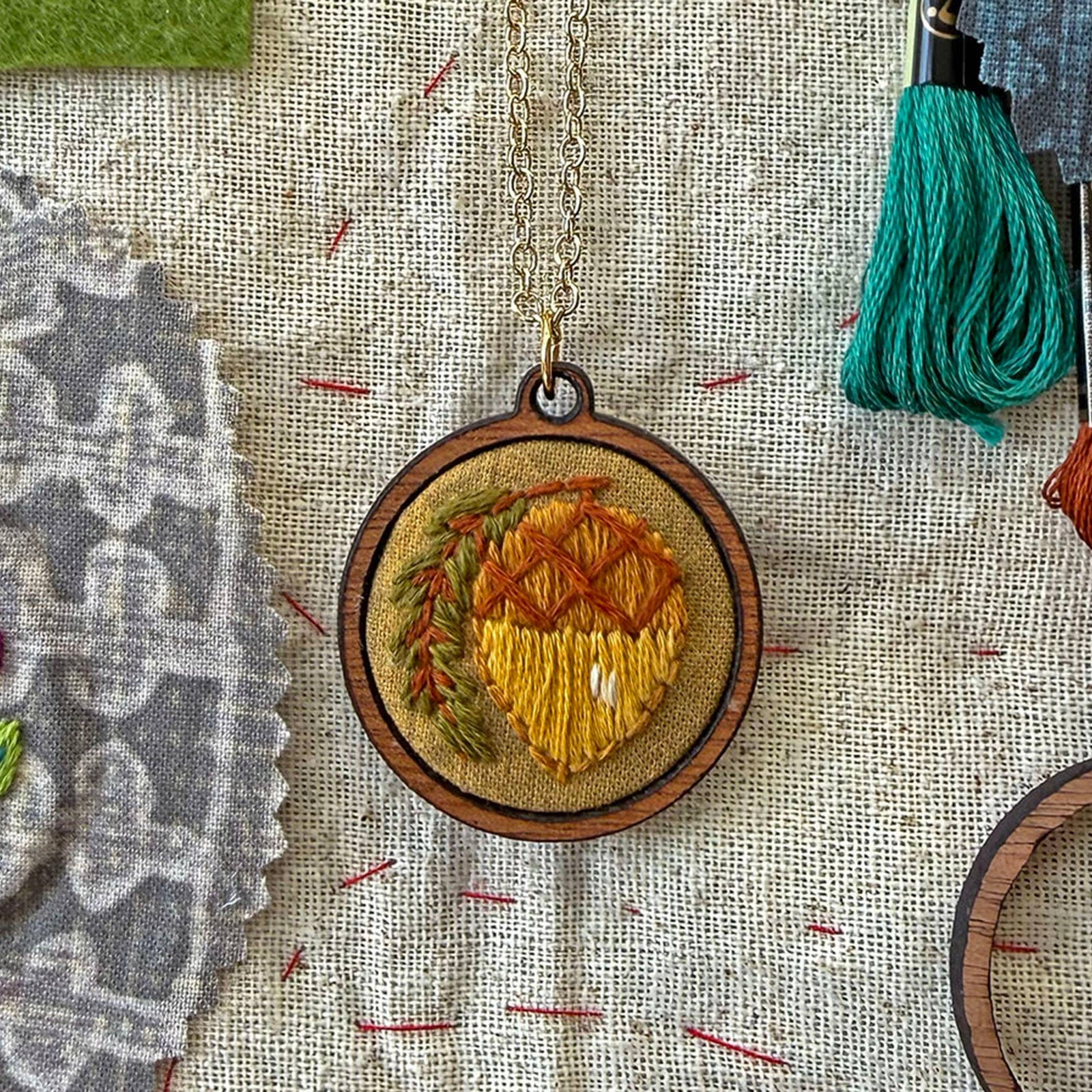 Wooden pendant with embroidered design on a textured fabric background
