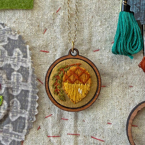 Wooden pendant with embroidered design on a textured fabric background