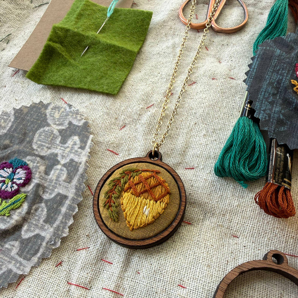 Embroidered necklace with fabric swatches and sewing tools on a textured surface