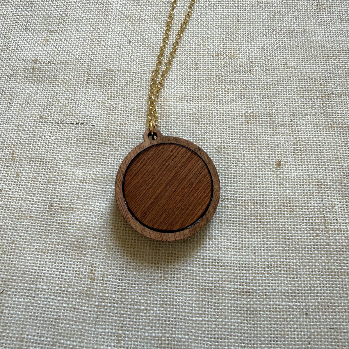 Back view of a wooden pendant necklace on a light fabric background