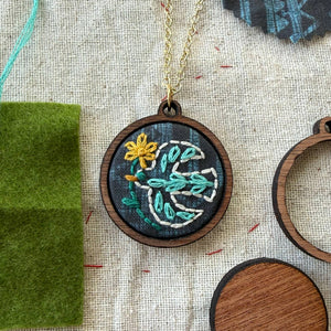 Embroidered necklace with bird design on a textured fabric background