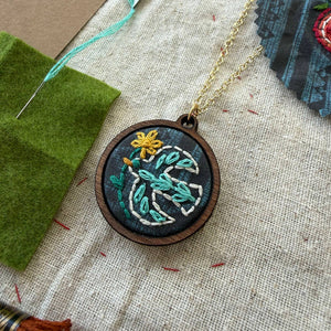 Embroidered necklace with floral bird design on a textured fabric background