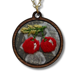 Necklace with a pendant featuring embroidered red cherries on a white background