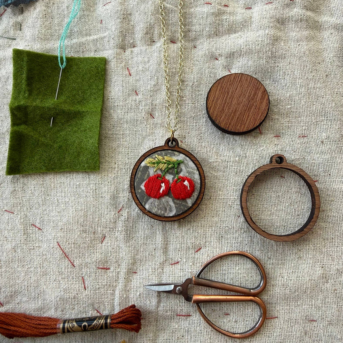 Handmade jewelry set with pendants, scissors, and embroidery tools on fabric background