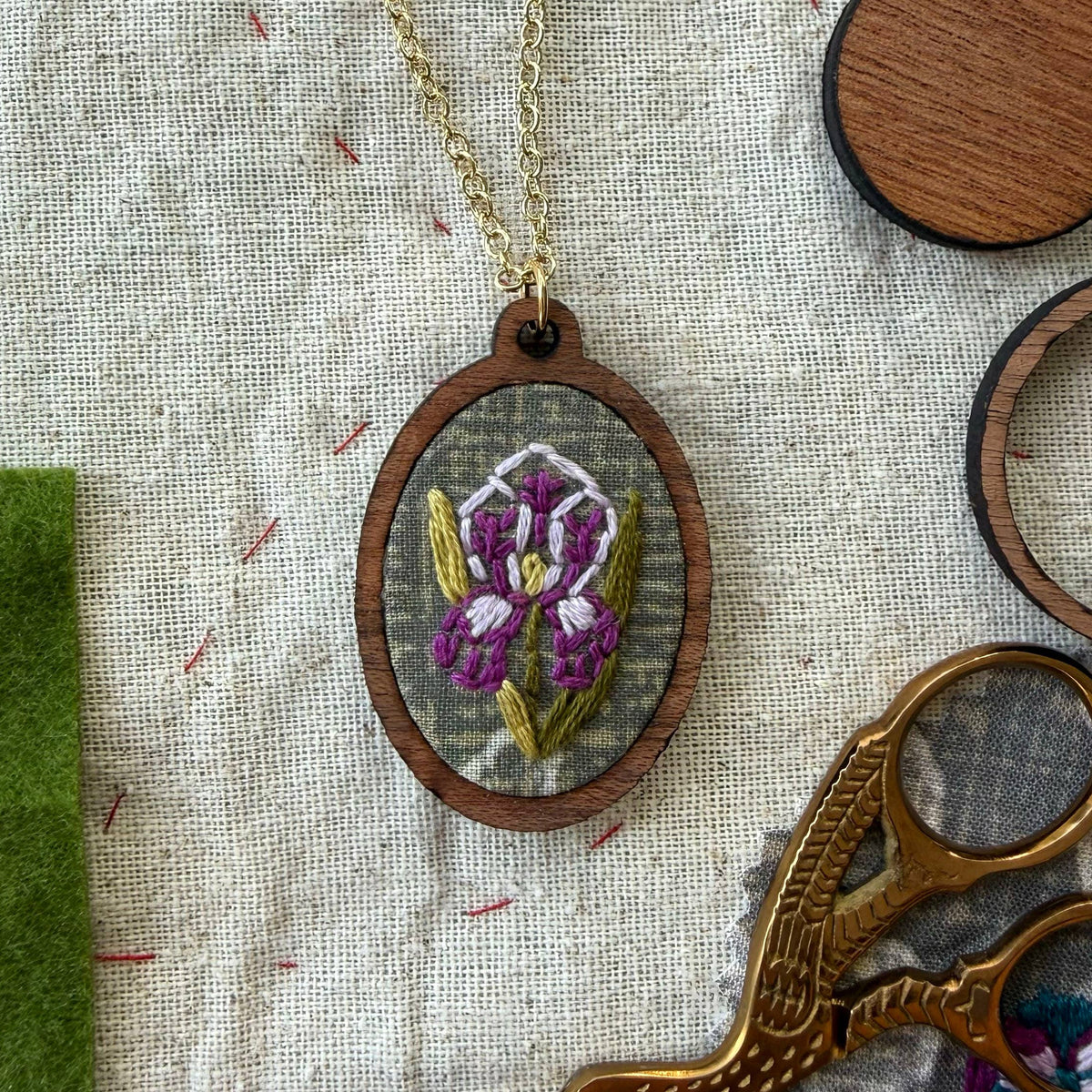 Embroidered pendant with a purple flower design on a fabric background with scissors and thread.