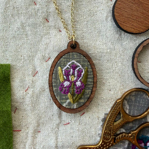 Embroidered pendant with a purple flower design on a fabric background with scissors and thread.