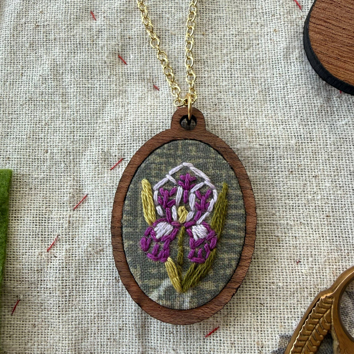 Embroidered pendant with a floral design on a chain, placed on a textured fabric background.