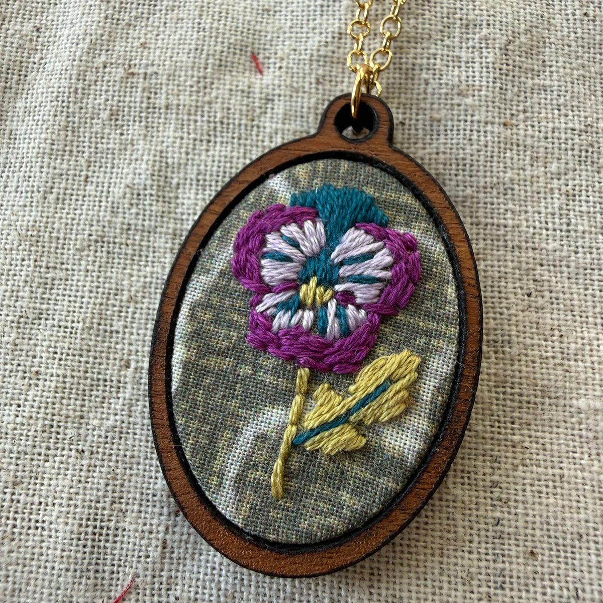 Embroidered flower pendant on a chain against a textured fabric background