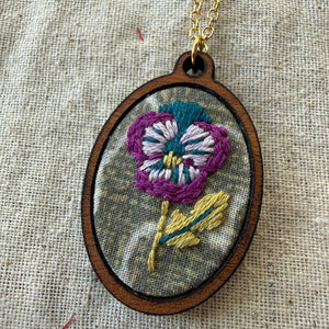 Embroidered flower pendant on a chain against a textured fabric background
