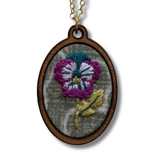 Embroidered flower pendant on a chain against a white background