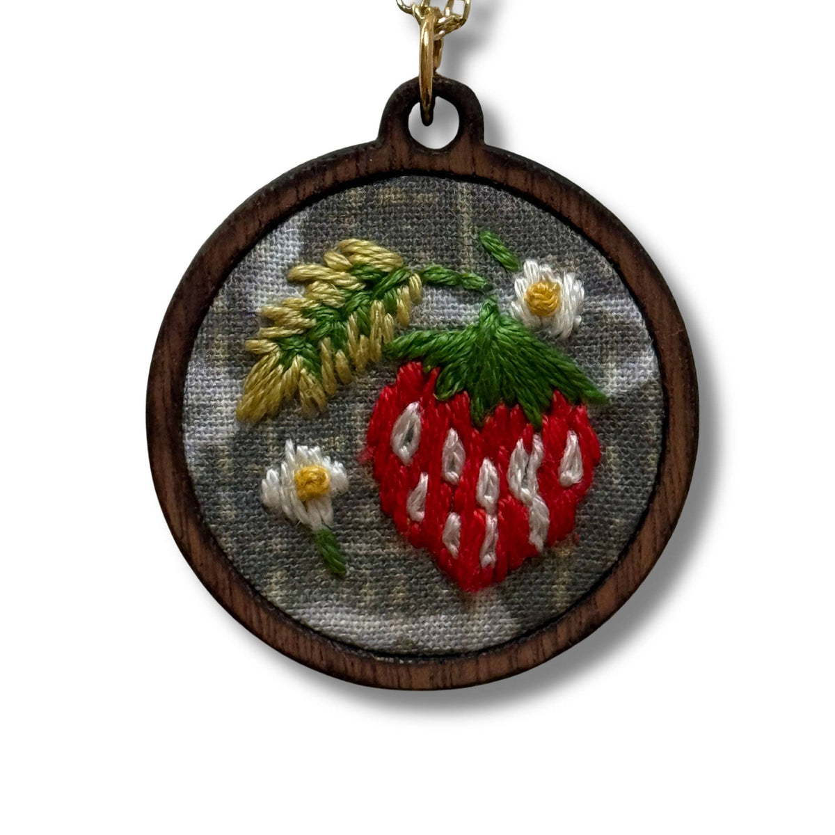 Necklace with embroidered pendant featuring a strawberry and floral design on a wooden background.