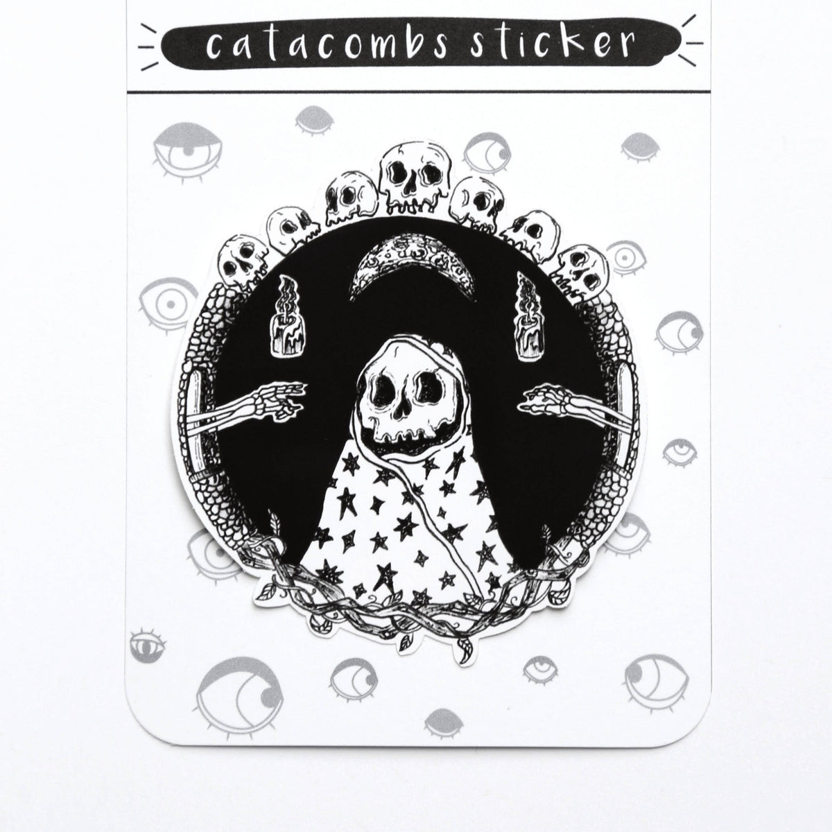 A gothic-themed sticker on its original backing card. The sticker features a black and white illustration of a hooded skeleton figure with stars on its cloak, surrounded by skulls, a crescent moon, and skeletal hands.