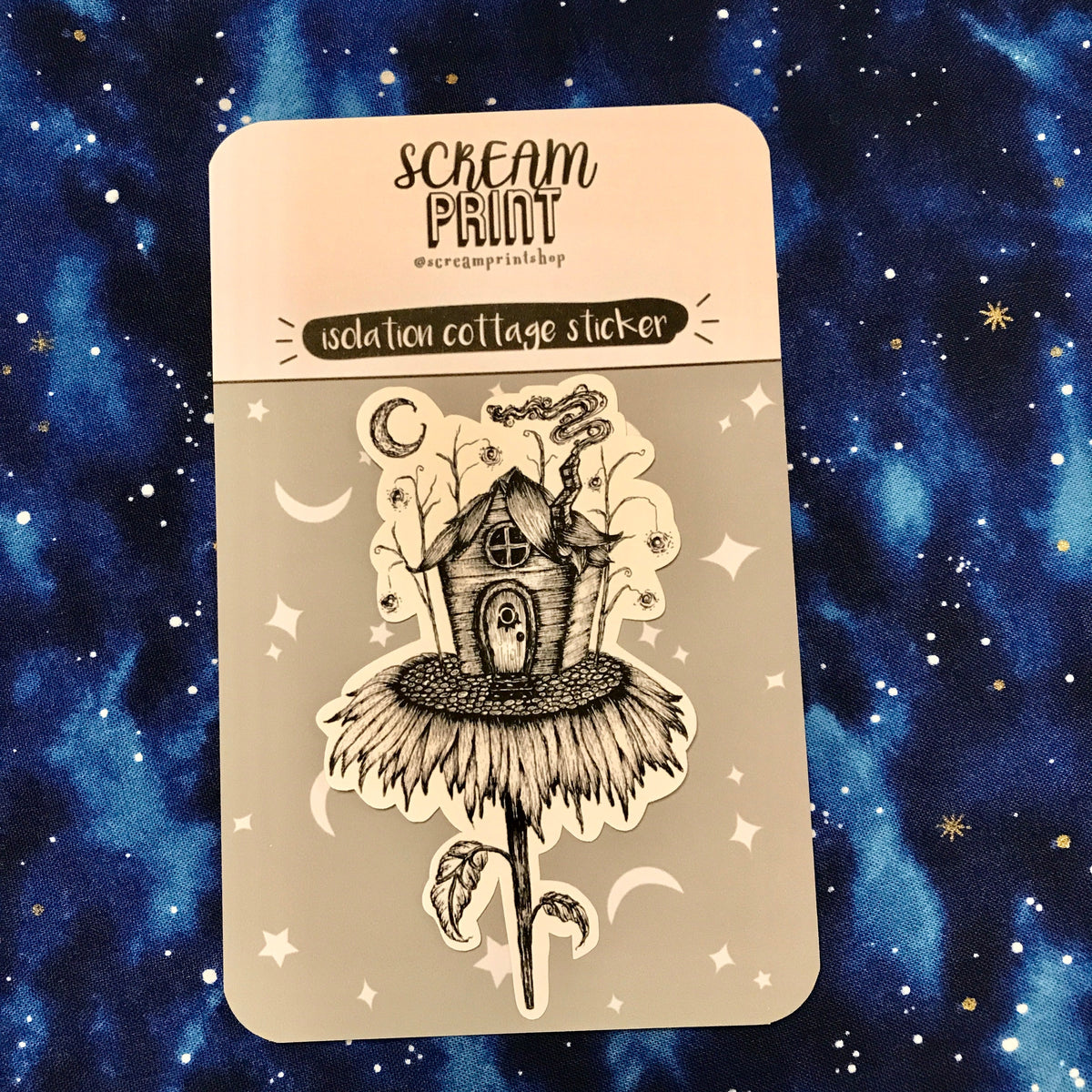 A sticker on a branded backing card of a tiny cottage on top of a sunflower with smoke coming out of the chimney and a crescent moon in the background. 