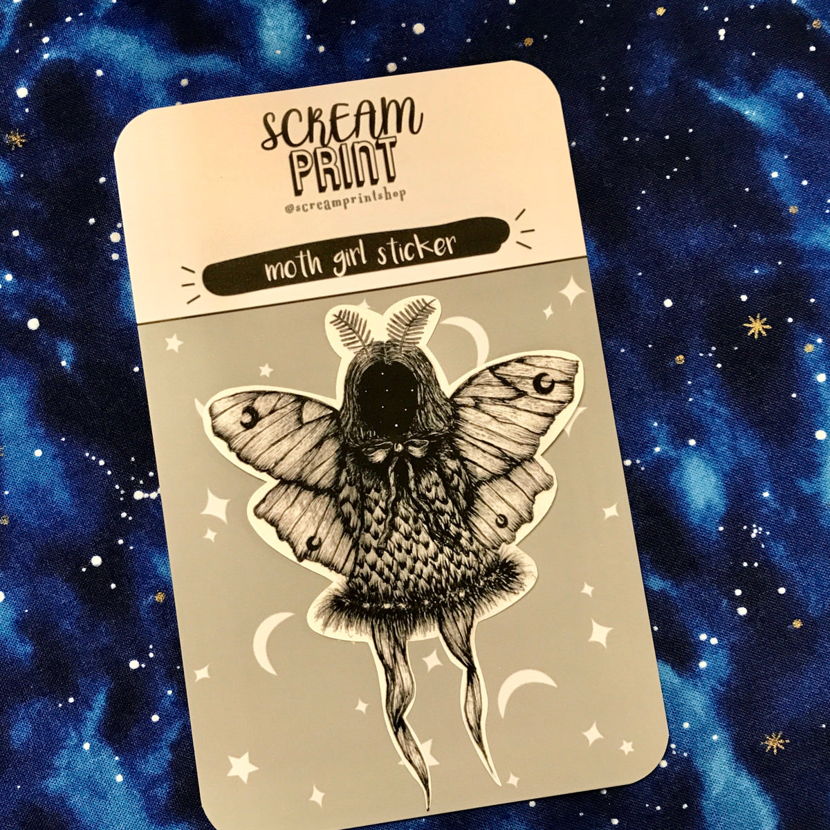 A black and white sticker of a creepy faceless girl with moth wings on a branded backing card.