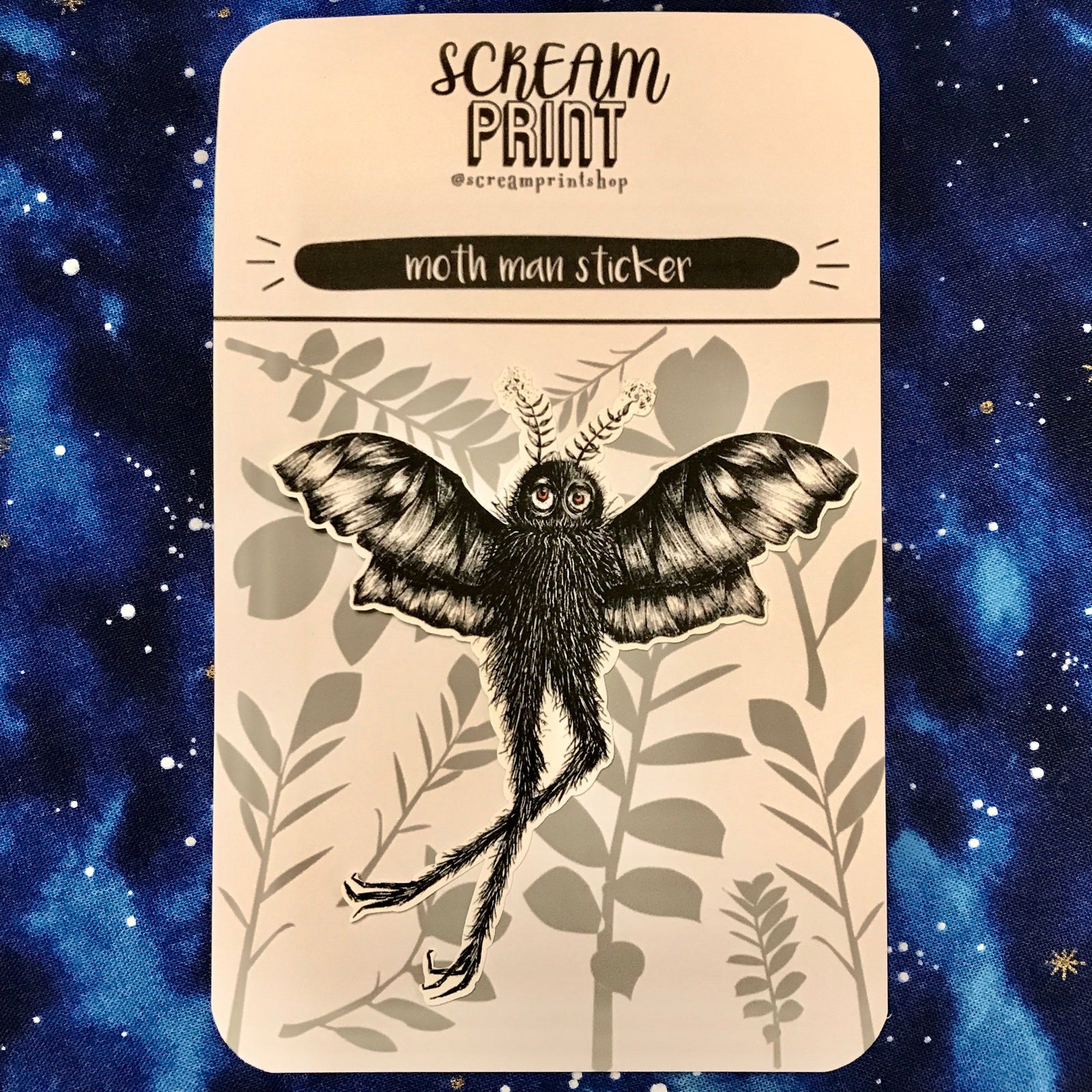 Black and white hand-drawn sticker of moth man on a branded backing card. 