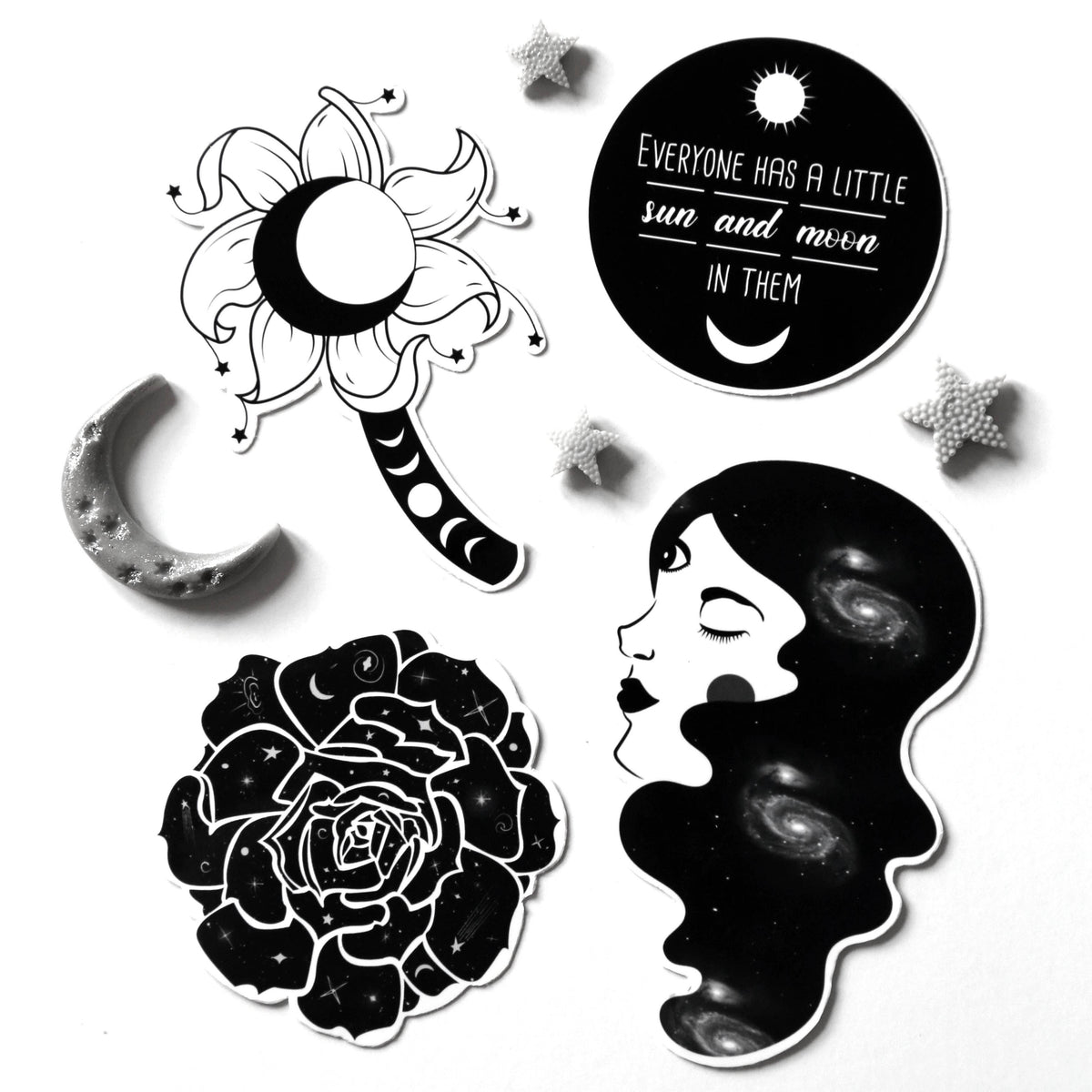 A set of black and white celestial-themed stickers on a white background, featuring a flower with a crescent moon, a moon phase wand, a circular quote sticker, a crescent moon, a rose, and a profile of a woman with galaxy hair.