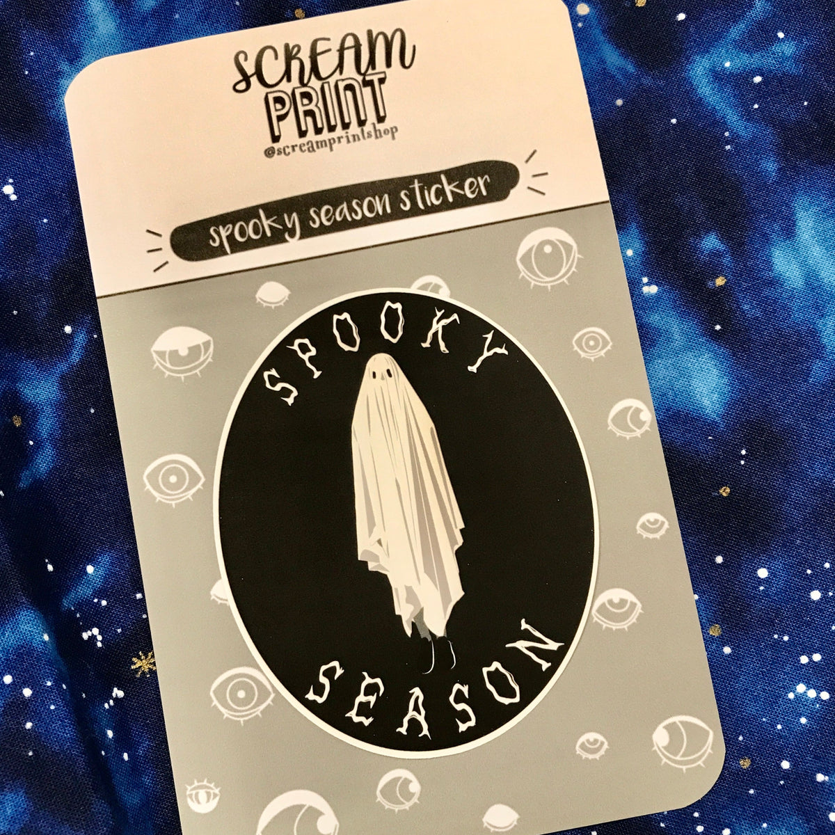 A black and white oval-shaped sticker with a ghost in the middle and text on the top and bottom that says "spooky season"