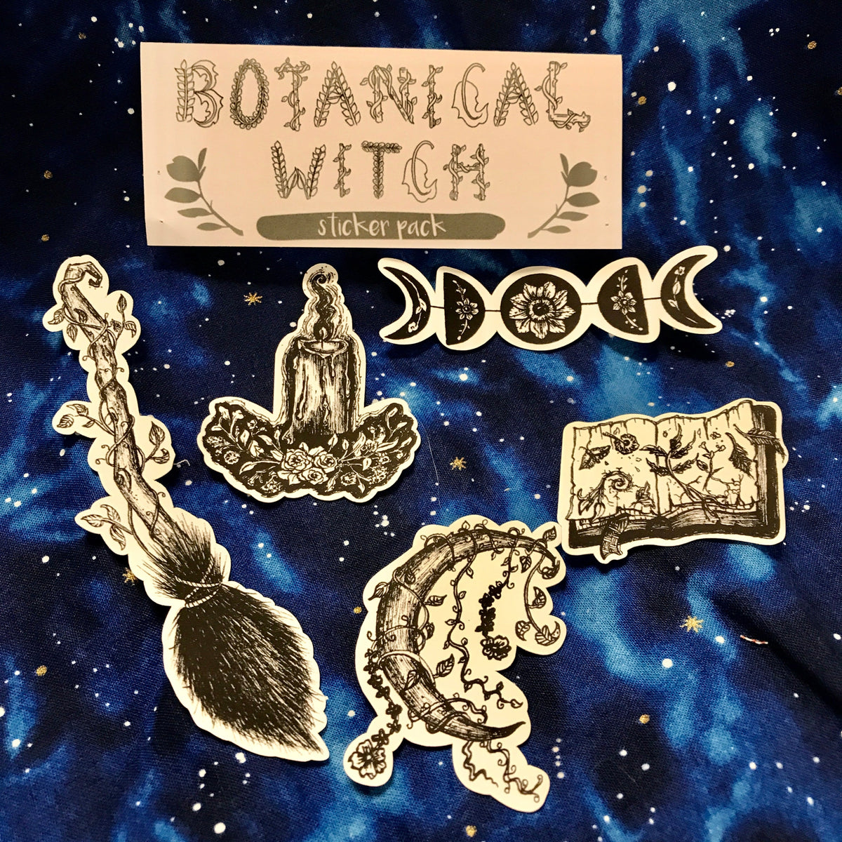 A grouping of five black and white illustrated stickers, including a broom, a candle, a crescent moon, a book, and a floral design, against a galaxy background 