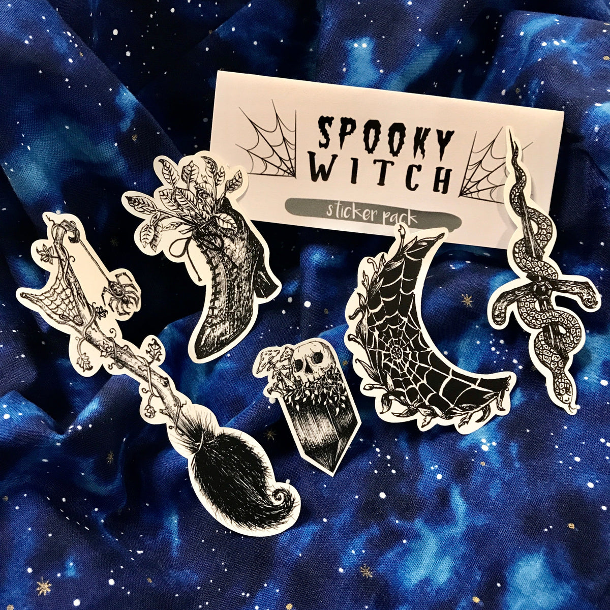A grouping of five hand-drawn black and white stickers, including a witch's broom, boot, crystal with a skull on top, crescent moon with a spiderweb, and snakes coiled around a dagger.