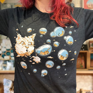 Person wearing a blue t-shirt with cartoon cat designs. There is a large cloud in the sky that looks like a giant cat head. The cat head is blowing bubbles that have tiny kitties inside. 