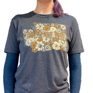 Person wearing a blue t-shirt with floral design and text that says "Don't Move Here" in a store setting. The floral design is in the shape of Washington state. 