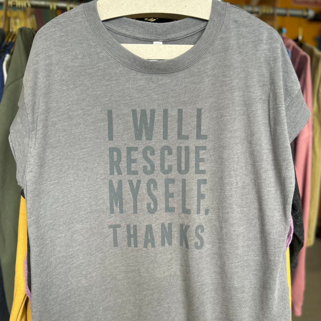 Gray t-shirt with 'I WILL RESCUE MYSELF. THANKS' text on a hanger in a store setting.