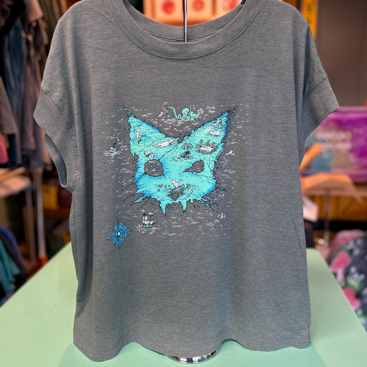 Washed basil t-shirt with a blue catographer graphic. It is a treasure map in the shape of a cat head. 