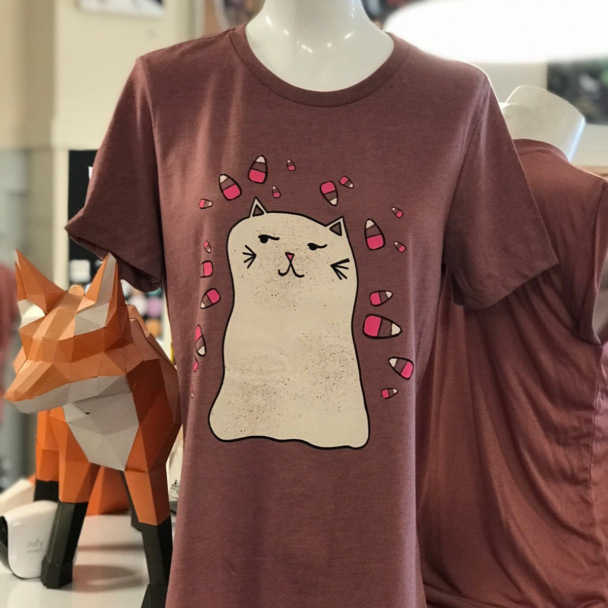 Heather mauve t-shirt with a ghost cat graphic on a mannequin in a store setting.